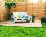 Ein gemütliches Palettensofa bauen: Ein hellblaues Sofa aus Paletten mit Kissen steht auf einer Holzterrasse im Garten.