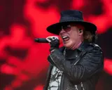 Axl Rose sjunger med en röd bakgrund. Trots rykten om axl rose sjukdom, levererar han en energisk show.