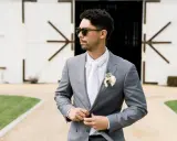 Man in a grey suit, white shirt, and tie, looking cool in sunglasses. Perfect for casual men's wedding guest attire in summer.