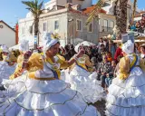 Menschen in Portugal feiern ausgelassen. Frauen in prachtvollen weißen und goldenen Kleidern mit Rüschen tanzen fröhlich.