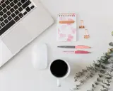Ein Schreibtisch mit Laptop, Maus, Notizbuch, Stiften und Kaffee. Ideal für Lehrer, die ihr Zeitmanagement verbessern wollen.