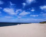 Pusta plaża z wydmami i latarnią morską, idealna na weekendowe odkrywanie magicznych miejsc nad Bałtykiem.