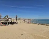 Sonniger Tag am Playa de la Mata. Menschen entspannen sich am Strand, einige im Wasser, andere unter Sonnenschirmen. Palmen säumen den Sand.