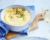 Cremige Polenta, verfeinert mit Butter und Kräutern, serviert in einer Schüssel. Ein Glas Weißwein und ein Holzbrett vervollständigen dieses Polenta Rezept.