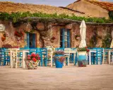 Taverna La Cialoma, un angolo incantevole di Siracusa e dintorni, con tavoli apparecchiati e sedie blu sotto un pergolato fiorito.