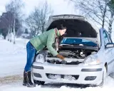 Kobieta w zimowej kurtce sprawdza silnik samochodu na śniegu. Zastanawia się, w jakiej temperaturze zamarza diesel, by uniknąć problemów.