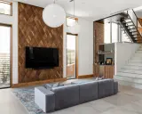 Nowoczesna ściana TV z drewna orzechowego, szara sofa i schody prowadzące na piętro.