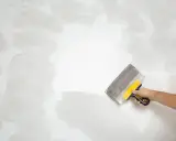 Mano con espátula aplicando masilla para alisar la pared, un paso clave en cómo quitar el gotele con espátula.