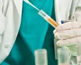 Badacz w białym fartuchu i rękawiczkach pobiera próbkę płynu do probówki. Badanie może pomóc ustalić, jak zahamować krwiomocz.