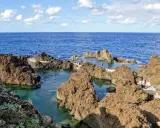 Naturschwimmbecken auf Madeira, umgeben von vulkanischem Gestein, mit Menschen, die die Sonne und das Meer genießen.