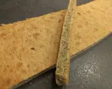 Deux fines tranches de biscuit joconde noisette, l'une posée sur l'autre, sur fond sombre.
