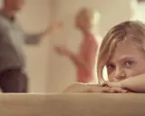 Niña asustada, escondida tras un sofá, mientras sus padres discuten delante de los hijos.