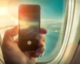 Dłoń trzyma smartfon, fotografując chmury z okna samolotu. Czy w samolocie można używać telefonu? Tak, do robienia zdjęć!