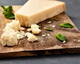 Ein Stück und zerbrochene Stücke von ist parmigiano parmesan liegen auf einem Holzbrett, garniert mit Minzblättern.