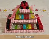 Tarta de chuches escalonada, con capas de gominolas de colores, marshmallows rosas y frutos rojos en la cima.