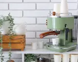 Máquina de café verde estilo retro, tazas apiladas y planta colgante. Un rincón del café listo para disfrutar.