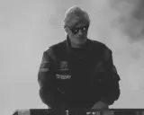 Młody artysta w okularach przeciwsłonecznych, w kurtce z naszywkami, gotowy do występu. Jego styl to czysty ras hip-hop.