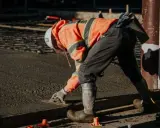 Obrero con casco y chaleco naranja trabajando con hormigón autocompactante, alisando la superficie con una llana.