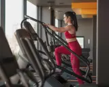 Frau macht ein Stairmaster Workout im Fitnessstudio. Sie trägt ein rotes Sportoutfit und trainiert intensiv.