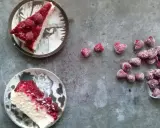 Dwa kawałki sernika z malinami na talerzach, obok garść mrożonych malin. Idealny deser na letnie popołudnie.