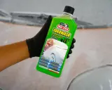 Mano con guanto nero tiene bottiglia di Idrowash, un detergente schiumoso verde brillante per auto.