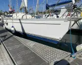 Un voilier blanc est amarré à quai. Le soleil se lève, projetant de longues ombres sur le ponton en bois.