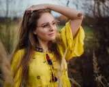 Portret dziewczyny w okularach i żółtej sukience, wśród traw. Różne rodzaje portretów w fotografii mogą uchwycić taką naturalną, swobodną chwilę.