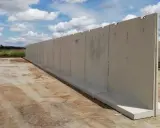 Larga pared de separador de hormigón prefabricado, instalada sobre una base de hormigón, con un cielo azul y nubes blancas al fondo.