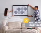 Pareja cuelga un cuadro moderno en pared de pladur. Un taladro descansa sobre el sofá, listo para la tarea.