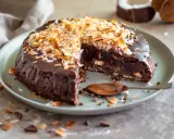 Kladdkaka med kokostosca, täckt med chokladglasyr och rostad kokos. En sked med chokladsås ligger bredvid.