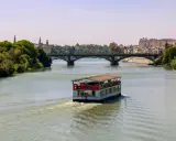 Ein Ausflugsboot fährt auf dem Guadalquivir, dem sevilla fluss, unter einer Brücke hindurch.