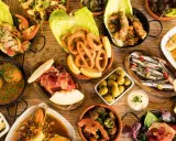 Vielfältige Tapas ideen: Tintenfischringe, Sardinen, Garnelen, Fleischbällchen, Schinken mit Melone, Oliven und mehr auf Holztisch.