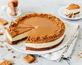 Ein köstlicher Lotus Cheesecake mit Karamellglasur und Keksbröseln. Ein Stück wurde bereits entnommen, daneben liegen weitere Kekse.