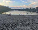 Zachód słońca nad stawem w Jelczu Laskowicach. Ludzie spacerują po piaszczystej plaży i kąpią się w wodzie.