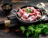 Piatto toscano con interiora di pollo crude in padella, con aglio, pepe e prezzemolo su tagliere di legno scuro.