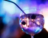 Ein Glas mit Eis und Beeren, in dem das tonic water leuchtet, vor einem verschwommenen, bunten Hintergrund.