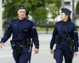 Dwóch policjantów w granatowych mundurach, mężczyzna i kobieta, idzie w stronę widza.