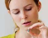 Kobieta trzyma niebieską kapsułkę, która może być jednym z leków z grupy benzodiazepiny.