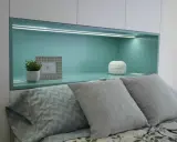 Habitación verde pistacho y gris con cama, almohadas y nicho iluminado.