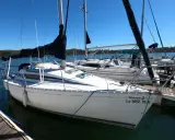 Voilier Beneteau First 235 blanc amarré à un ponton en bois, avec voiles noires et bleues.