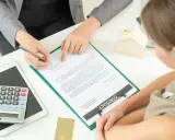 Kobieta podpisuje umowę, rozważając wspólny kredyt bez ślubu a rozstanie. Obok leży kalkulator i model domu.
