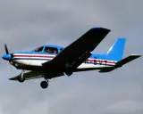Blau-weiße Piper PA mit roten Streifen fliegt im Himmel.