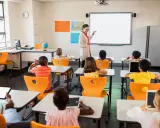 Nauczycielka prowadzi lekcję w klasie pełnej dzieci. To idealne miejsce do nauki pedagogiki przedszkolnej i wczesnoszkolnej w Poznaniu.