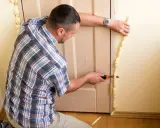 Hombre corta poliuretano expandido sobrante alrededor de un marco de puerta.