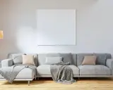 Sofá gris con cojines en tonos tierra y grises, mantas y planta. El color de cojines para sofá gris ideal para un ambiente acogedor.