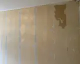 En vägg med gul tapet som lossnat på flera ställen, med synliga limrester och sprickor.