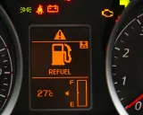 Na desce rozdzielczej świeci się kontrolka paliwa z napisem "REFUEL". Wskaźnik pokazuje niski poziom paliwa, sugerując, że rezerwa ile km zostało do przejechania jest niewielka.