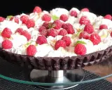 Pyszna tarta czekoladowa z malinami, udekorowana bitą śmietaną i listkami mięty. Idealna na deser.