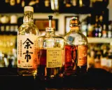 Tre flaskor japansk sprit, inklusive Nikka Whisky From The Barrel och Yoichi, står uppradade på en mörk yta.