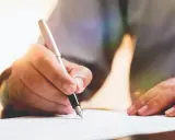 Dłoń pisze piórem po papierze, przygotowując dokument. Dowiedz się, jak napisać testament.